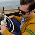 Man with big black glasses driving a classic car